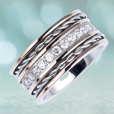 A close-up of the Aficionado Rose Gold Ring featuring stainless steel and two-tone plating with a row of sparkling stones and twisted metal accents, designed for unisex wear.