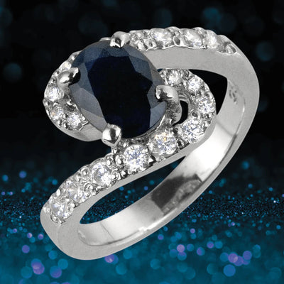 Sapphire Meander Ring featuring a sterling silver band with rhodium plating, showcasing a deep blue sapphire centerpiece surrounded by sparkling clear stones.