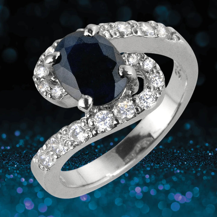 Sapphire Meander Ring featuring a sterling silver band with rhodium plating, showcasing a deep blue sapphire centerpiece surrounded by sparkling clear stones.