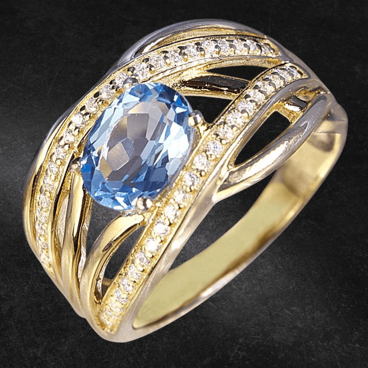 Ophelia Topaz Ring featuring a blue topaz center stone set in sterling silver with gold plating and accented by sparkling clear stones, designed for women’s jewelry.