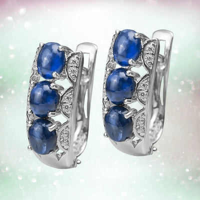 Berry Sapphire Earrings featuring three oval blue sapphire stones set in rhodium-plated sterling silver with sparkling accent stones, designed for women’s jewelry.