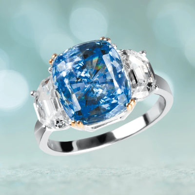 Sapphira Ring featuring a large cushion-cut blue gemstone flanked by two clear emerald-cut stones set in sterling silver with two-tone plating, designed for women.