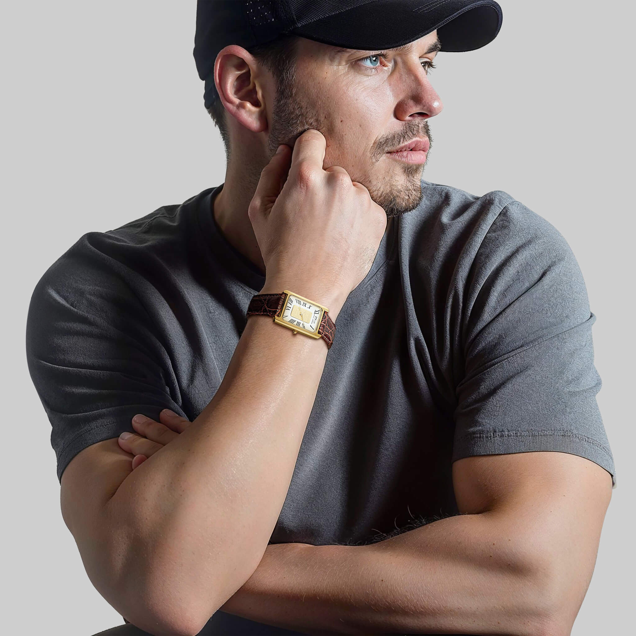 Man wearing a Gold Ingot Men's Watch with a gold-plated stainless steel case and white dial, paired with a brown leather strap, dressed in a grey t-shirt and black cap.