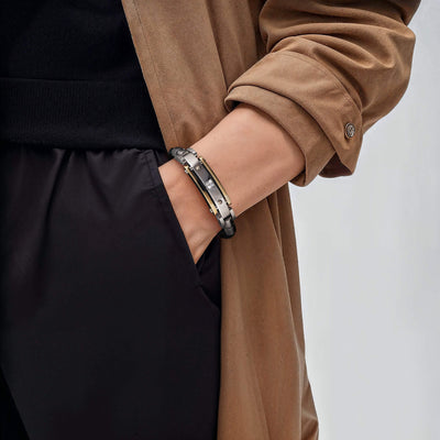 Close-up of a person wearing the Men's Diamond Leather Bracelet featuring steel and leather materials with a two-tone plating color, styled with a brown coat and black pants.