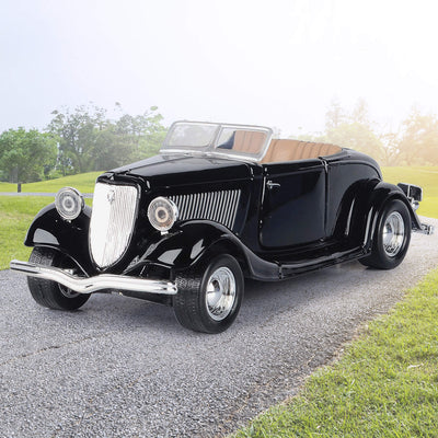 Black vintage convertible car with a glossy finish parked on a gravel driveway beside a green lawn and trees
