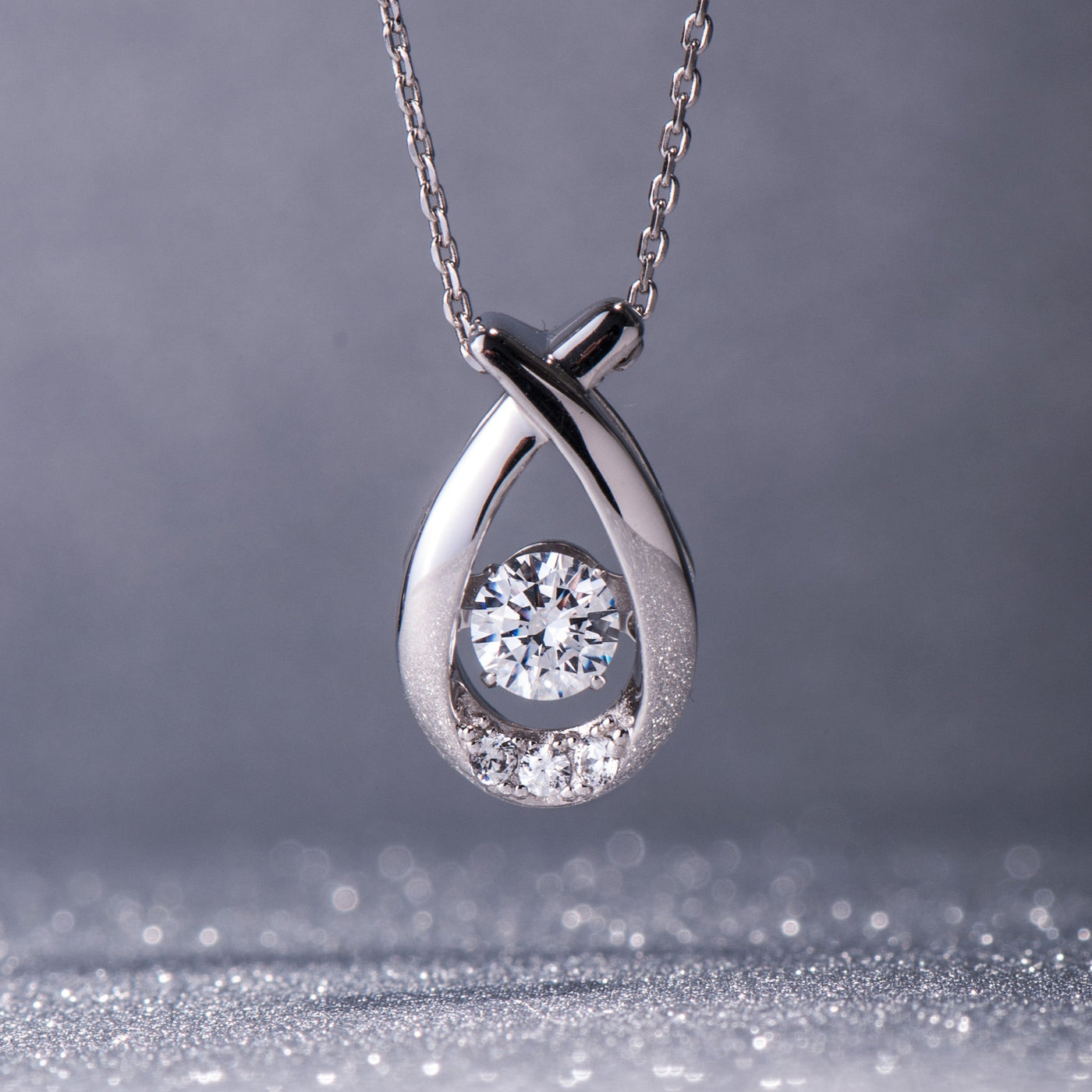 Silver teardrop-shaped pendant with a diamond on a gray background
