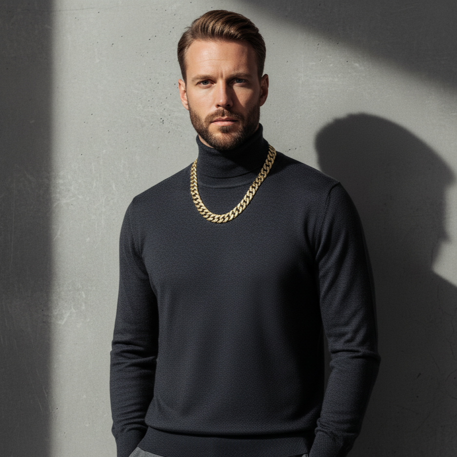 Man wearing a dark turtleneck sweater with a gold chain necklace against a gray wall.