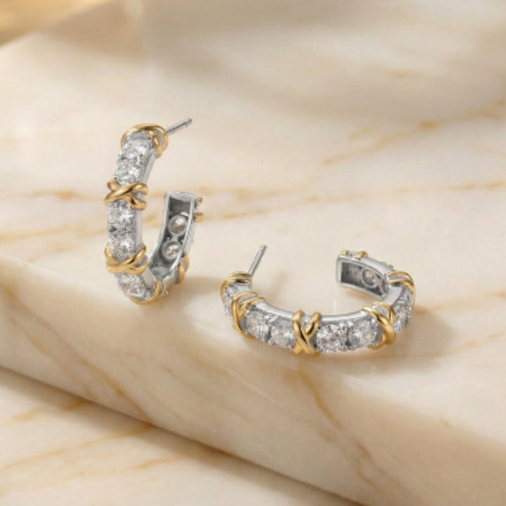 Pair of gold and silver hoop earrings on a beige marble surface