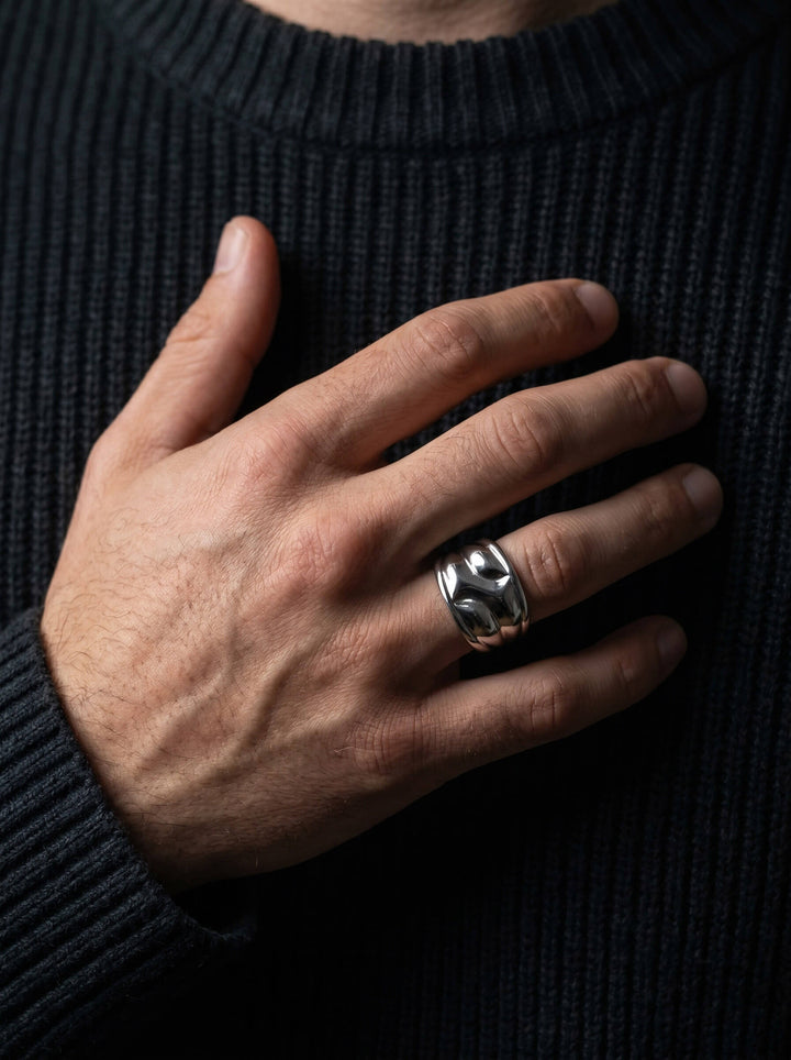 Close-up of a man's hand wearing the Axis Interlock Men’s Ring made of polished silver-tone metal on the ring finger against a dark ribbed sweater background.