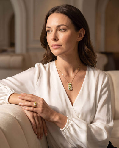 Elegant woman wearing a white blouse showcasing the Elysian Peridot Ring and matching pendant, highlighting exquisite jewelry with Up To 75% Off Retail.