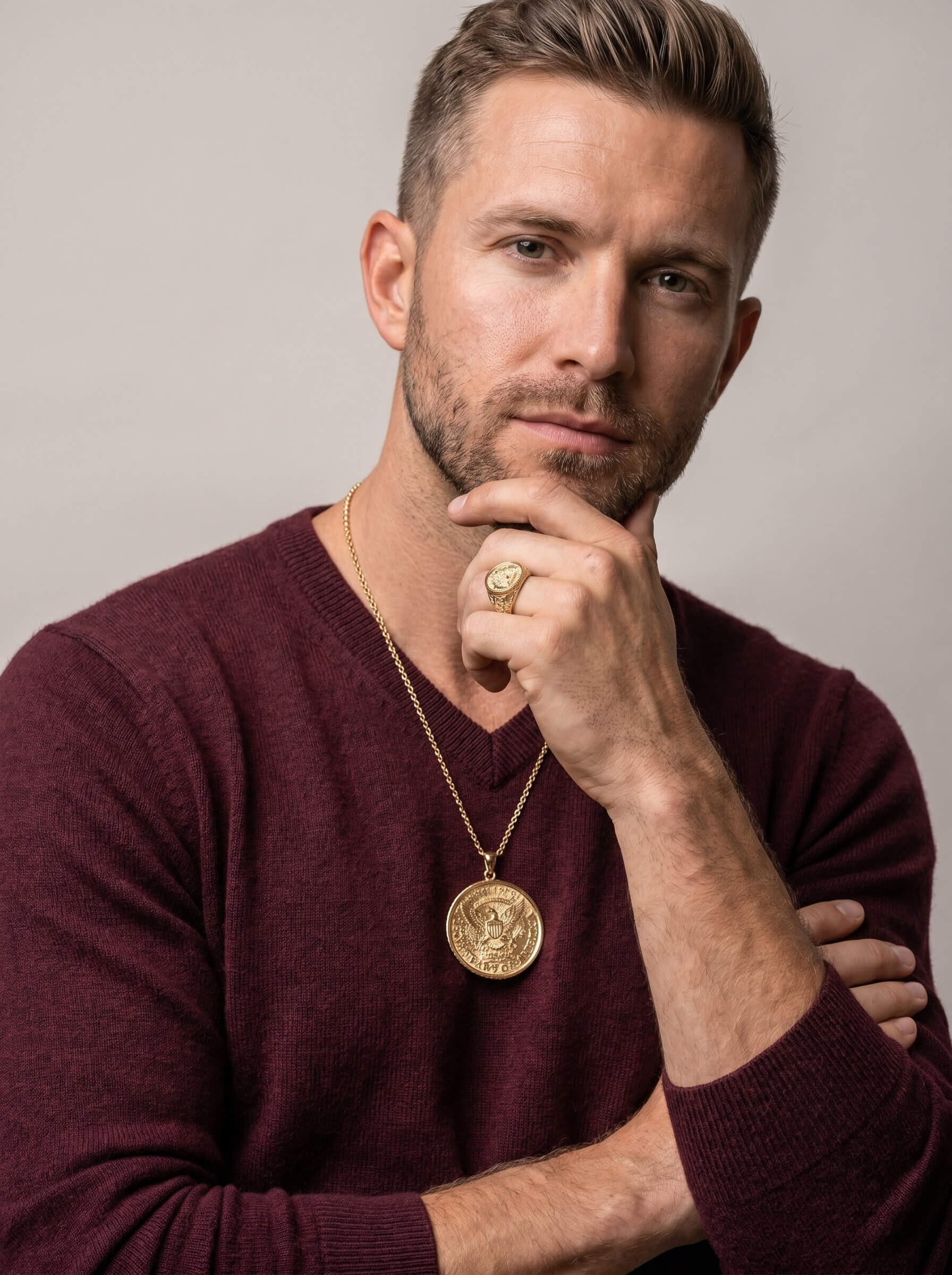 Man wearing a gold pendant necklace and matching ring with an eagle emblem, styled with a burgundy sweater, showcasing the American Glory Collection jewelry set.