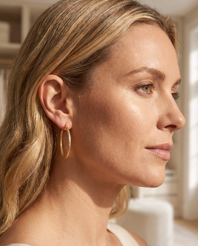 Close-up of a woman wearing the Lucente Hoop Set, featuring elegant gold hoop earrings that add a sophisticated touch to her look in a softly lit indoor setting.