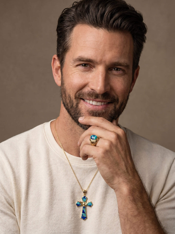 Smiling man wearing a gold necklace and ring with vivid blue gemstones from the Wings Of Freedom Collection, showcasing elegant jewelry pieces for men.
