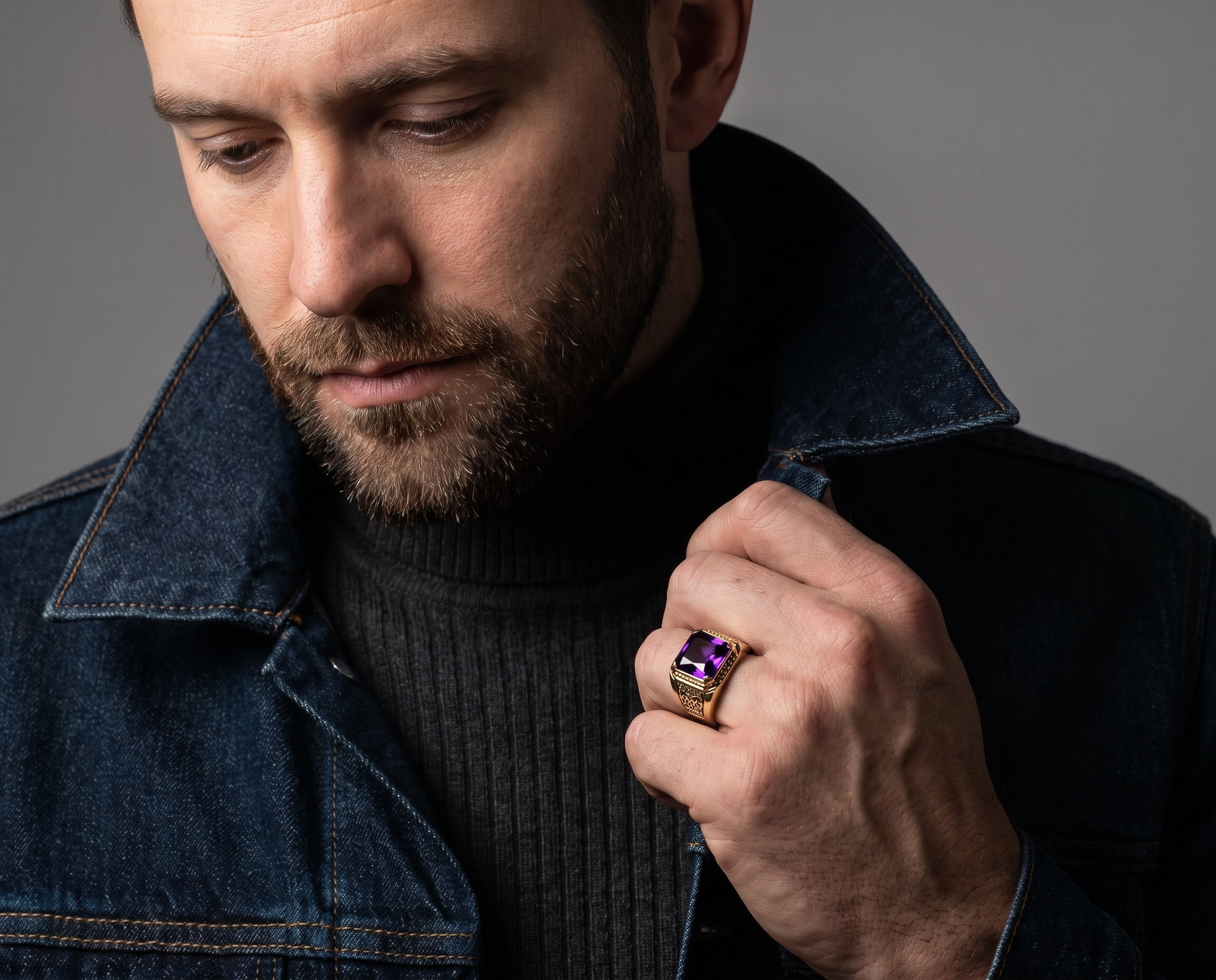 Augustus Purple Ring with a vivid purple gemstone on a mans hand as he wears a dark denim jacket and black knit sweater