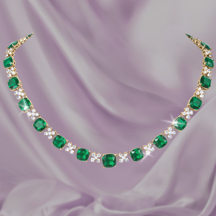 Freya Necklace with vibrant emerald green gemstones clear crystal accents and a gold tone setting displayed on soft lavender fabric Up To 75% Off Retail