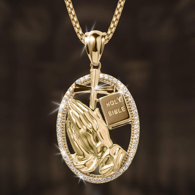 Holy Pendant featuring a gold-tone oval frame with sparkling stones, containing praying hands, a cross, and a Holy Bible design on a matching chain necklace.
