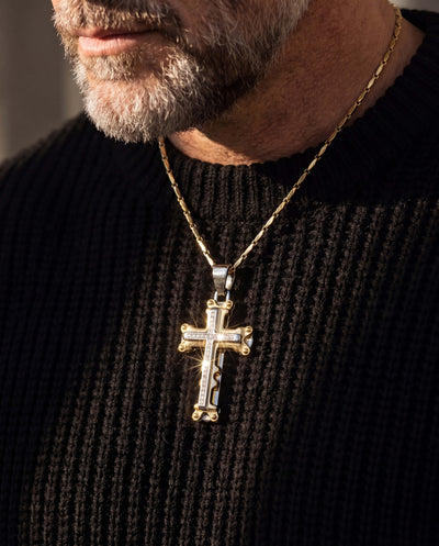 Close-up of a male wearing a Goliath Steel Cross Pendant made of stainless steel with a two-tone plating on a gold chain against a black textured sweater.