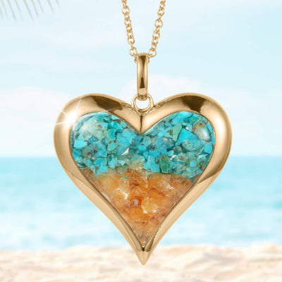 Sunlit Shore Heart Pendant featuring a gold-tone heart-shaped frame with turquoise and amber stone inlays on a delicate chain, set against a beach background.