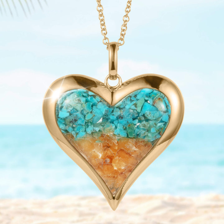 Sunlit Shore Heart Pendant featuring a gold-tone heart-shaped frame with turquoise and amber stone inlays on a delicate chain, set against a beach background.