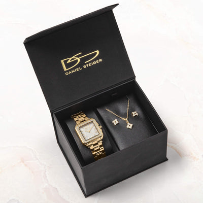 Open black Daniel Steiger presentation box displaying a gold-tone watch with a square face alongside a delicate necklace and matching earrings