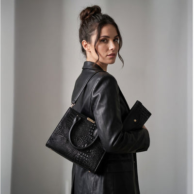 A woman in a black leather jacket carries a black crocodile-embossed leather handbag and matching clutch against a neutral gray background. Gabriella Bag Collection featuring a black crocodile texture handbag wallet and mini purse with polished gold accents Up To 75% Off Retail