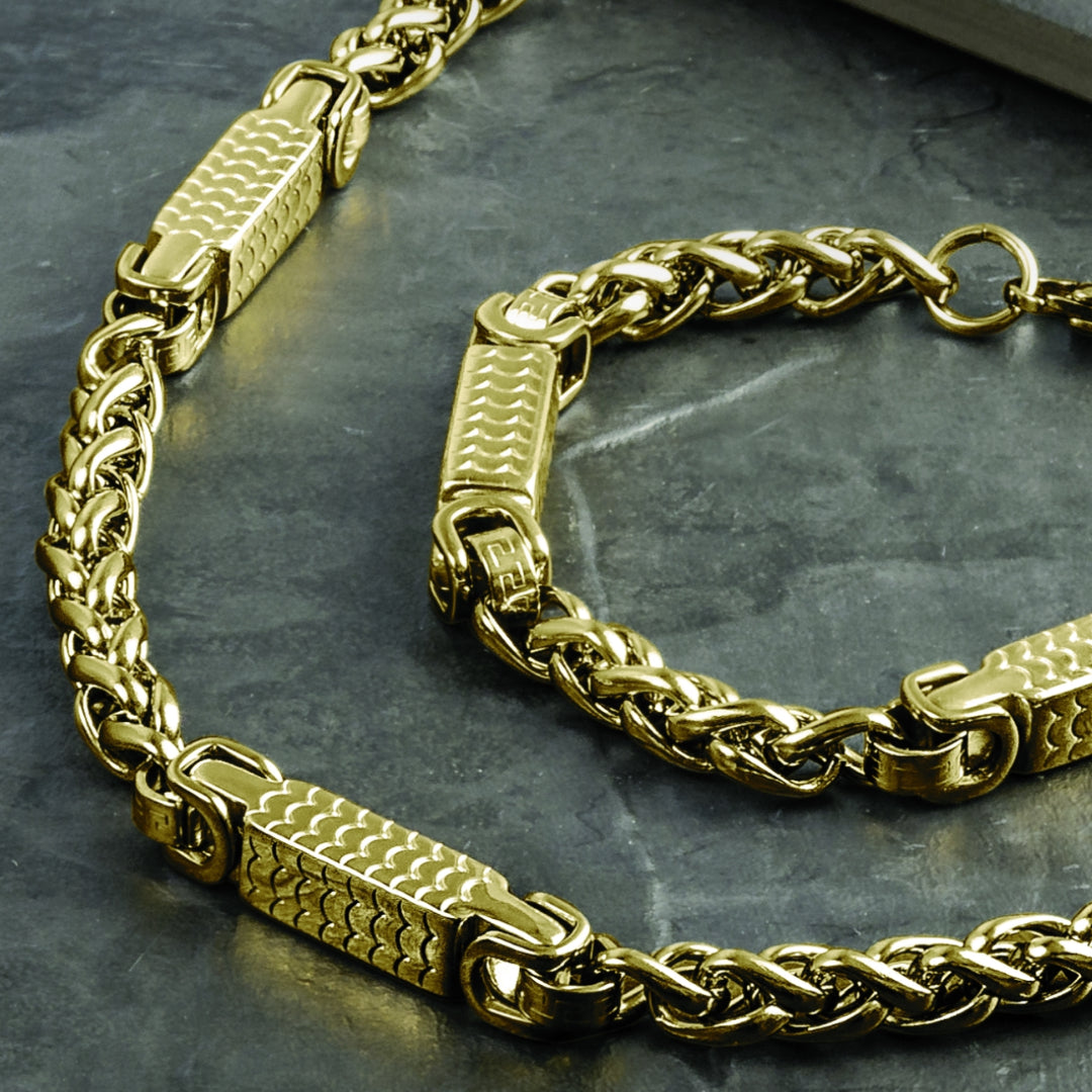 Close-up of Arco Men's Necklace in gold plated stainless steel featuring a braided chain design with textured rectangular links on a dark stone surface.