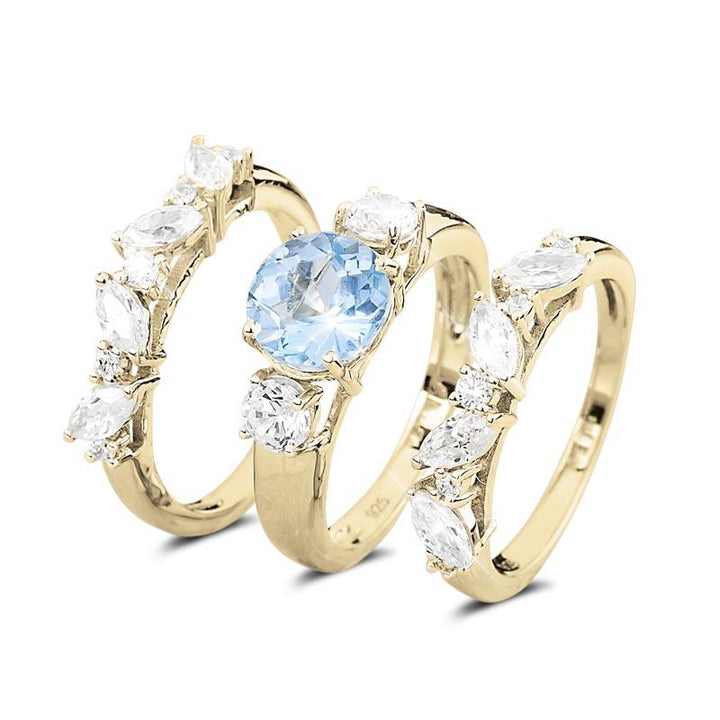 Isla Blue Topaz Trio Bridal Ring featuring a sterling silver gold-plated design with a central blue topaz and sparkling clear stones, elegant female jewelry ring set.